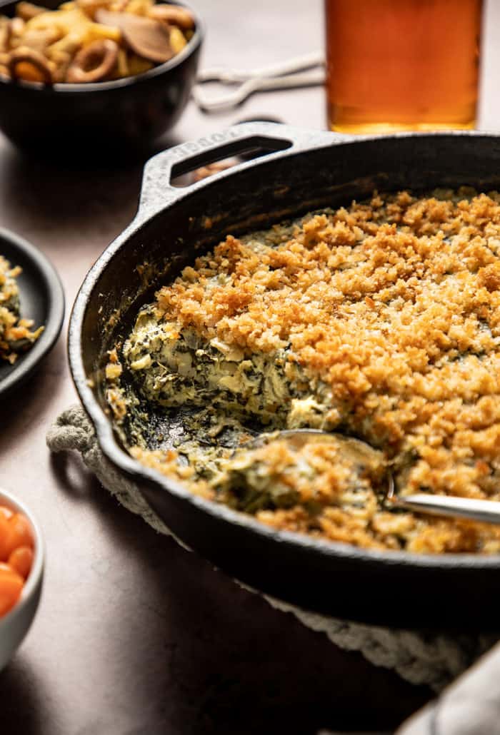 Spoon resting in a skillet where spinach artichoke dip has just been served out