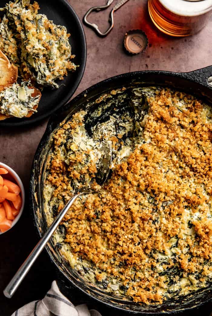 Overhead view of spoon dishing out spinach artichoke dip from a skillet