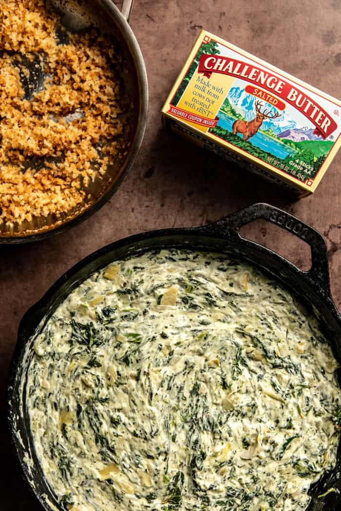Spinach artichoke dip in a cast iron skillet next to a bowl of toasted panko breadcrumbs