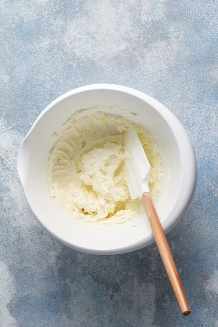 Cream cheese and butter whipped together in a white mixing bowl set on a blue countertop
