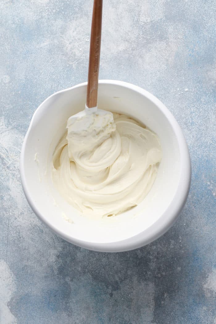 Freshly made cream cheese frosting in a white mixing bowl with a spatula in it