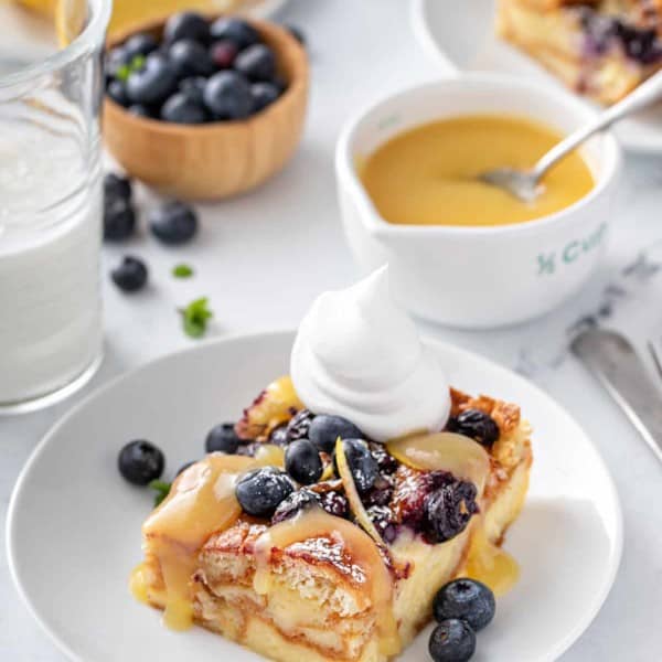 Plated slice of blueberry bread pudding topped with lemon curd, fresh blueberries, and whipped cream