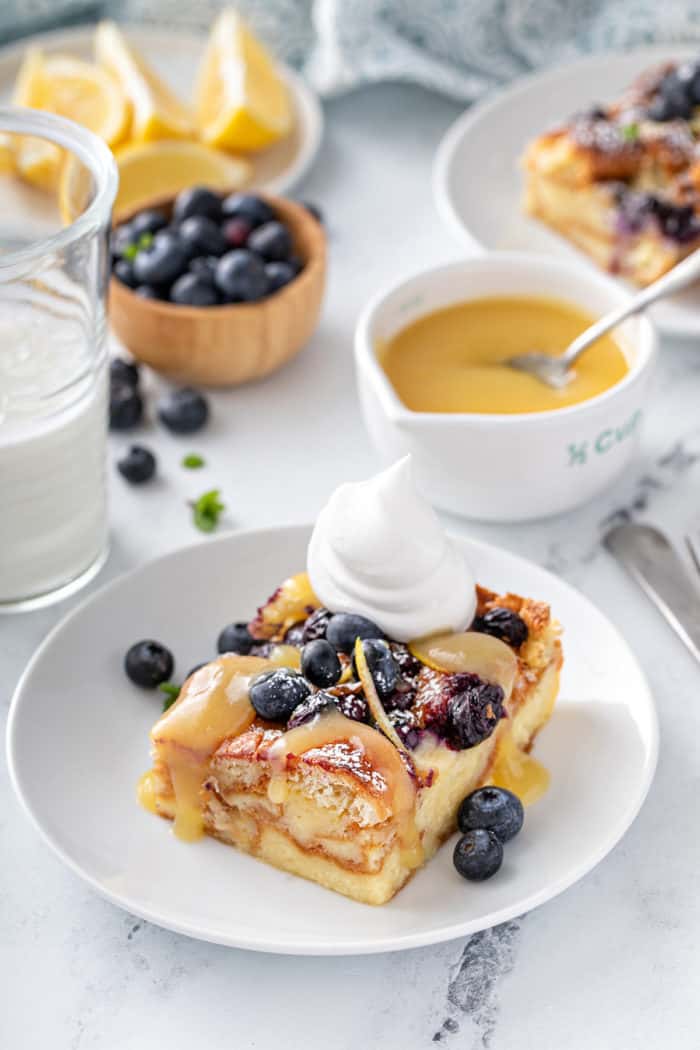 Plated slice of blueberry bread pudding topped with lemon curd, fresh blueberries, and whipped cream