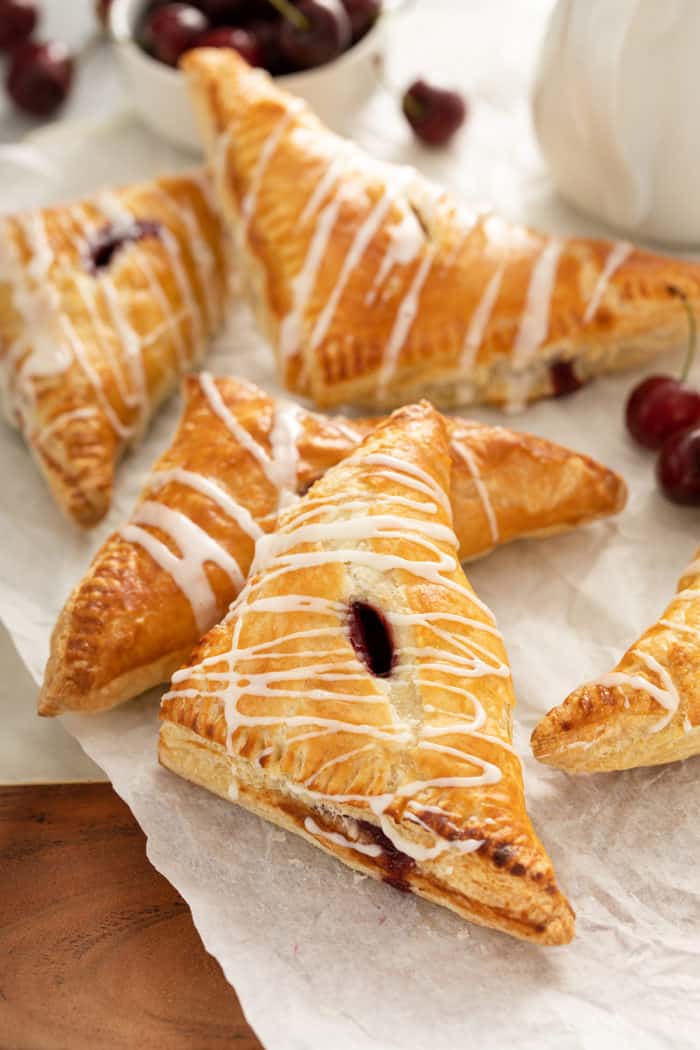 Cherry turnovers topped with glaze scattered on a piece of parchment paper