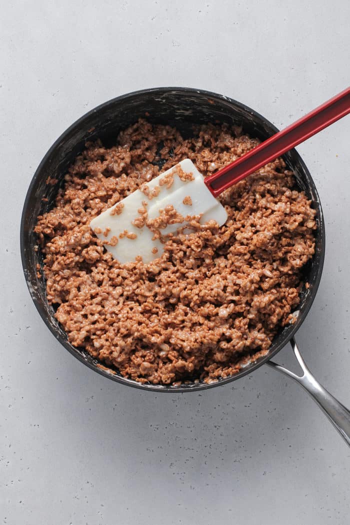 Spatula stirring cocoa krispies cereal into melted marshmallows