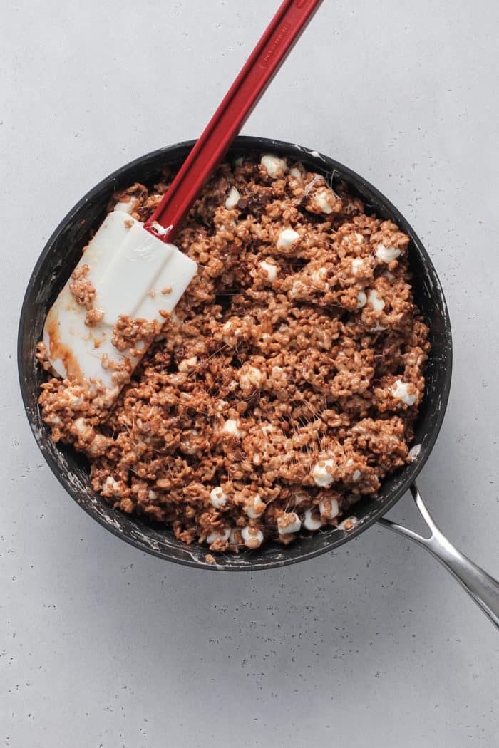 Chocolate rice krispie treat mixture, speckled with mini marshmallows, being stirred together in a saucepan