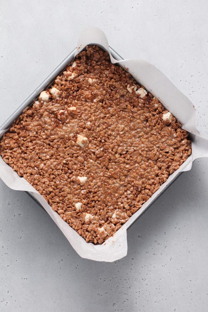 Chocolate rice krispie treats gently pressed into a parchment-lined pan