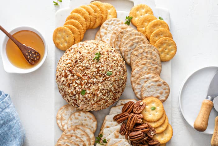 Overhead view of a classic cheese ball on a cutting board surrounded by various crackers and and whole pecans