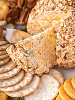 Close up of a wedge of classic cheese ball being cut out of the whole cheese ball