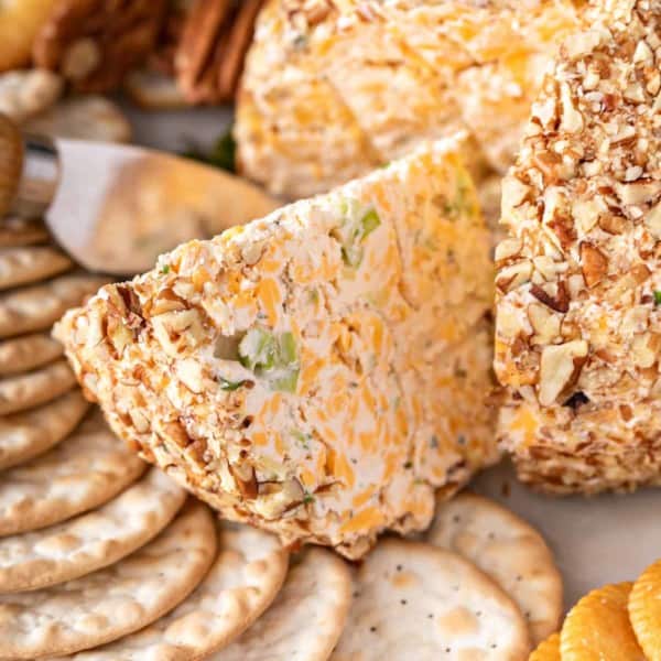 Close up of a wedge of classic cheese ball being cut out of the whole cheese ball