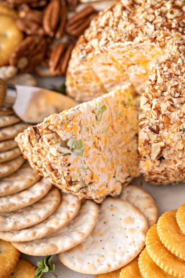 Close up of a wedge of classic cheese ball being cut out of the whole cheese ball