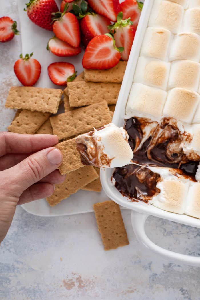 Hand scooping up s'mores dip with a piece of graham cracker