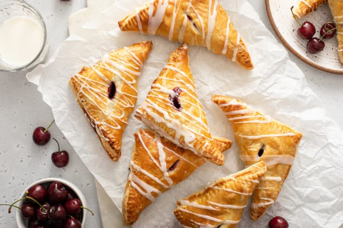 Overhead view of glazed cherry turnovers arranged on a piece of parchment paper