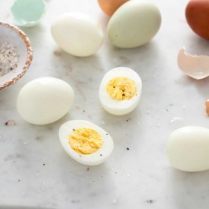 Two hard boiled egg halves on a marble surface, surrounded by whole hard boiled eggs