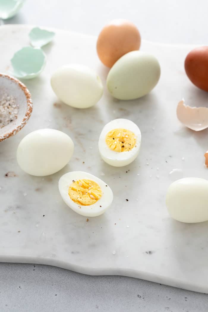 Two hard boiled egg halves on a marble surface, surrounded by whole hard boiled eggs