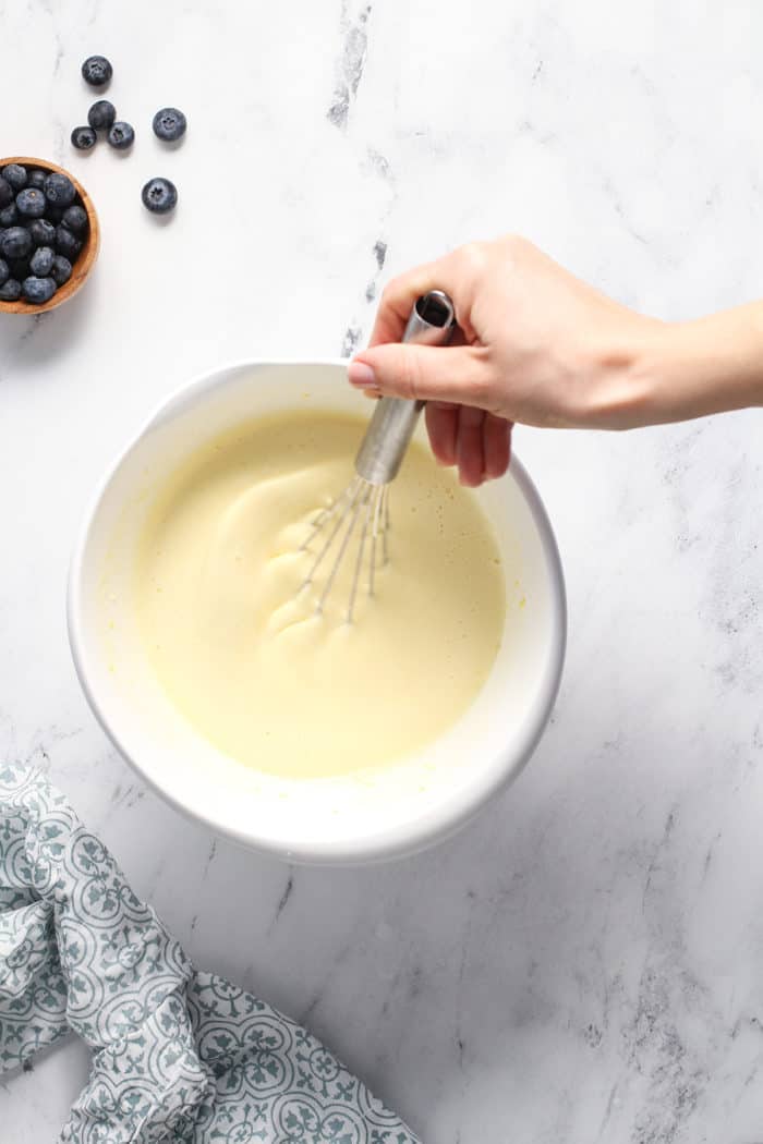 Hand whisking custard for blueberry bread pudding in a white bowl