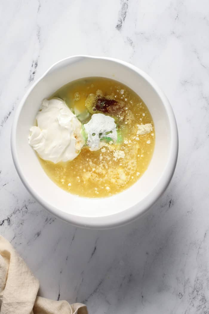 Ingredients for pistachio pudding cake in a white mixing bowl on a marble countertop