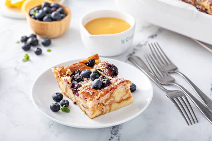 Slice of blueberry bread pudding, dusted with powdered sugar, on a white plate