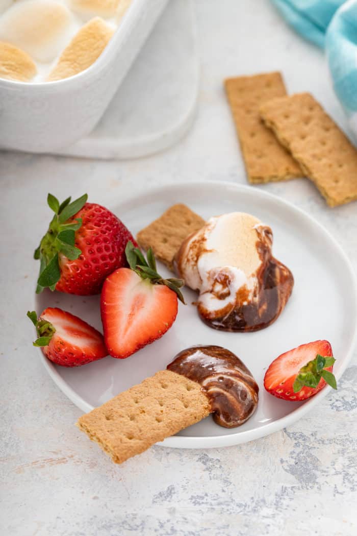 S'mores dip on a white plate with graham crackers and fresh strawberries