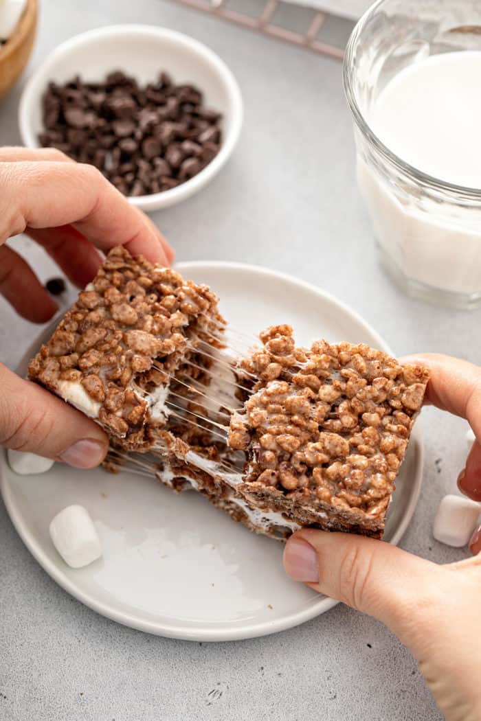 Hand pulling apart a chocolate rice krispie treat to show the soft, gooey middle