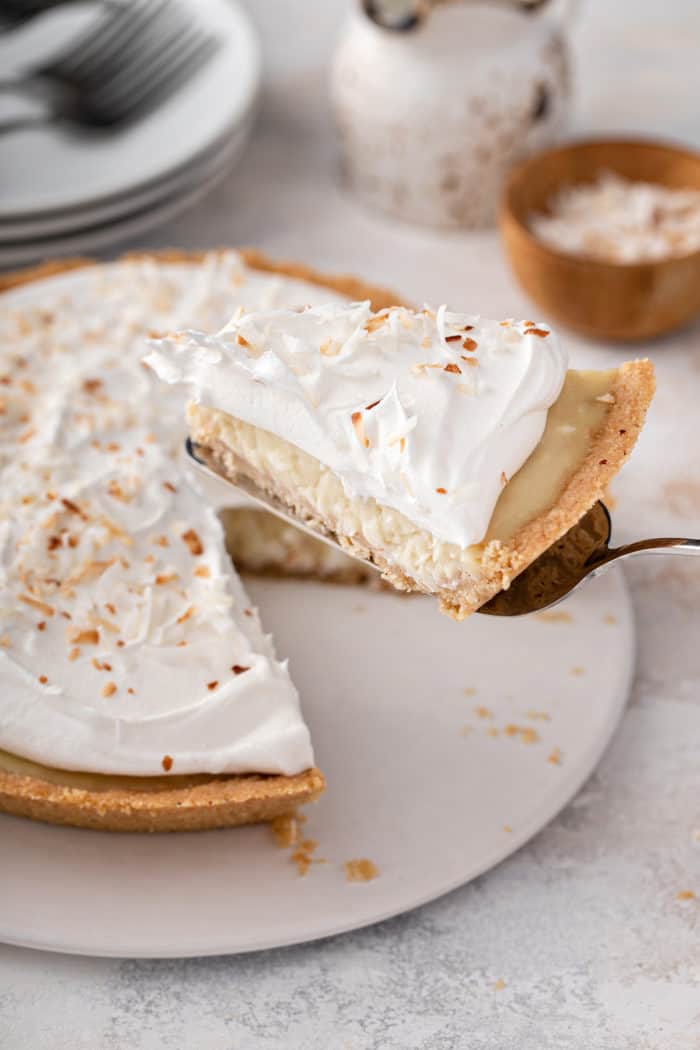 Pie server removing a slice of pie from a coconut cream pie on a white platter