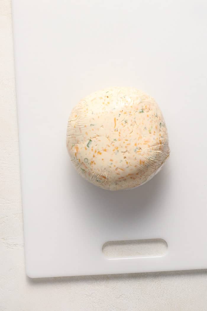 Cheese ball mixture shaped into a ball and wrapped in plastic wrap