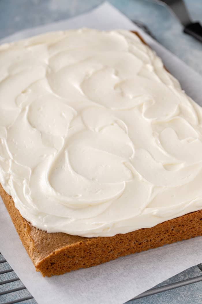 Spatula with cream cheese frosting on it set on the side of a white mixing bowl