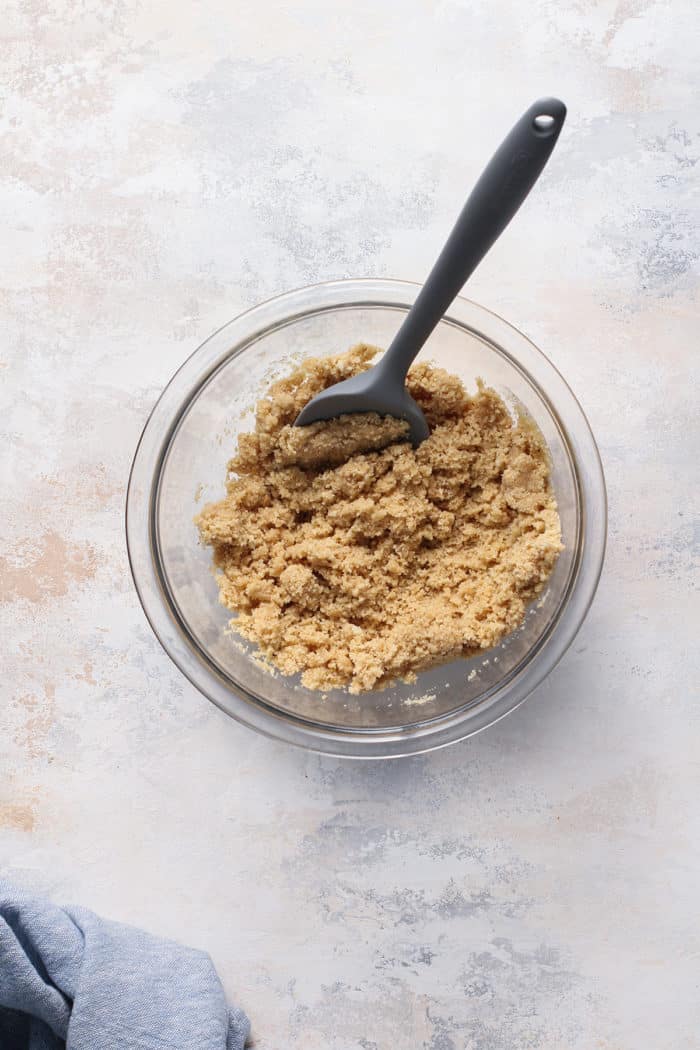 Spatula stirring the ingredients for a shortbread cookie crust in a glass bowl