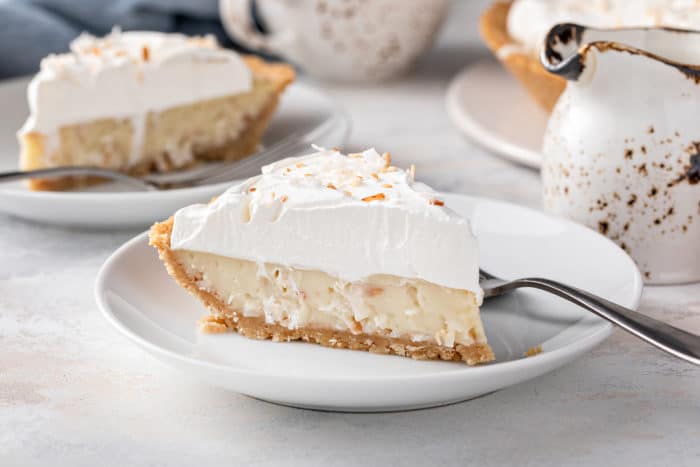 Side view of a slice of coconut cream pie on a white plate, showing the layers of filling and whipped cream