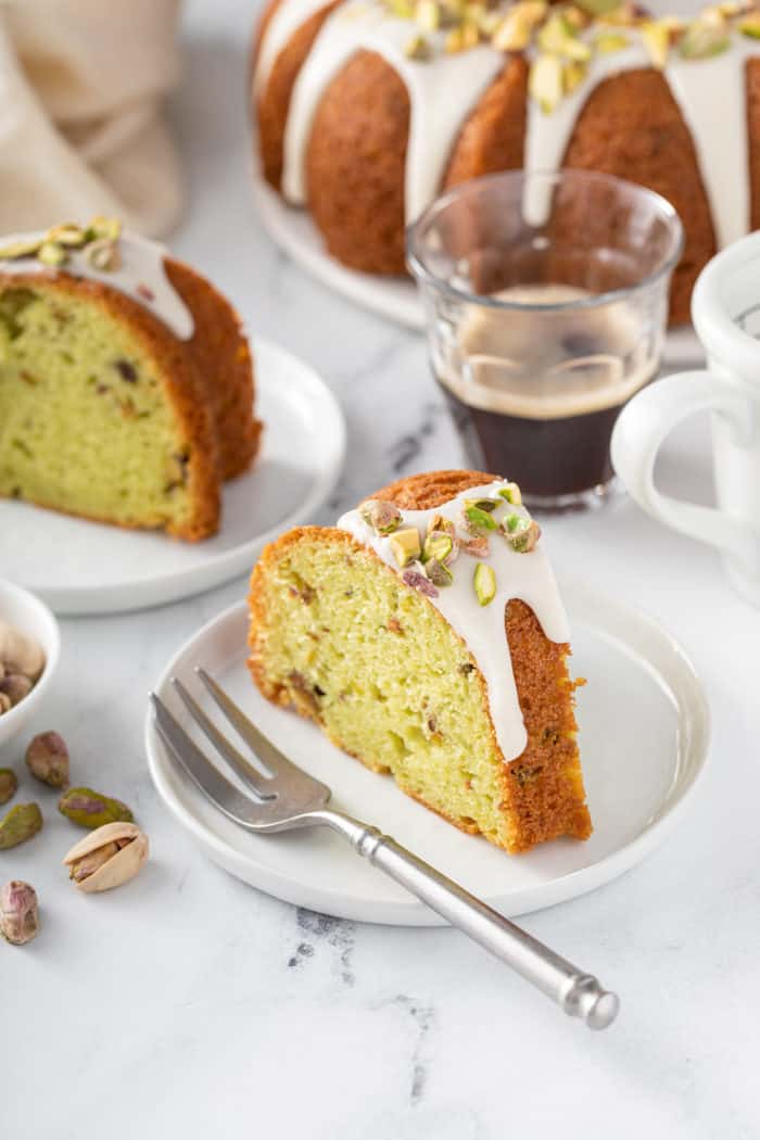 Slice of pistachio pudding cake set next to a fork on white plate, with more slices of cake in the background