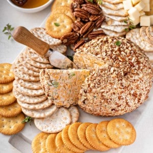 Cheese ball on a white board surrounded by crackers, with a wedge being cut from it