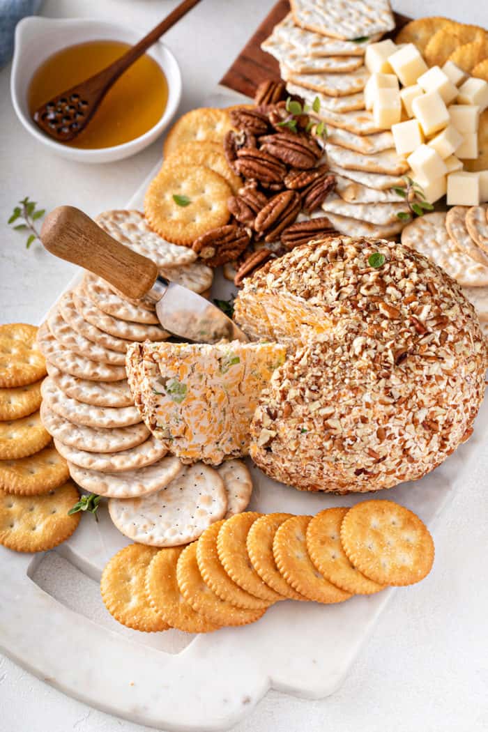 Cheese ball on a white board surrounded by crackers, with a wedge being cut from it