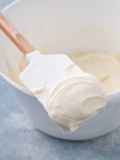 Spatula with cream cheese frosting on it set on the side of a white mixing bowl