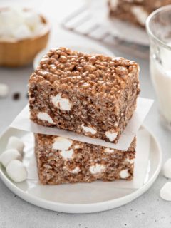 Two chocolate rice krispie treats stacked on a white plate