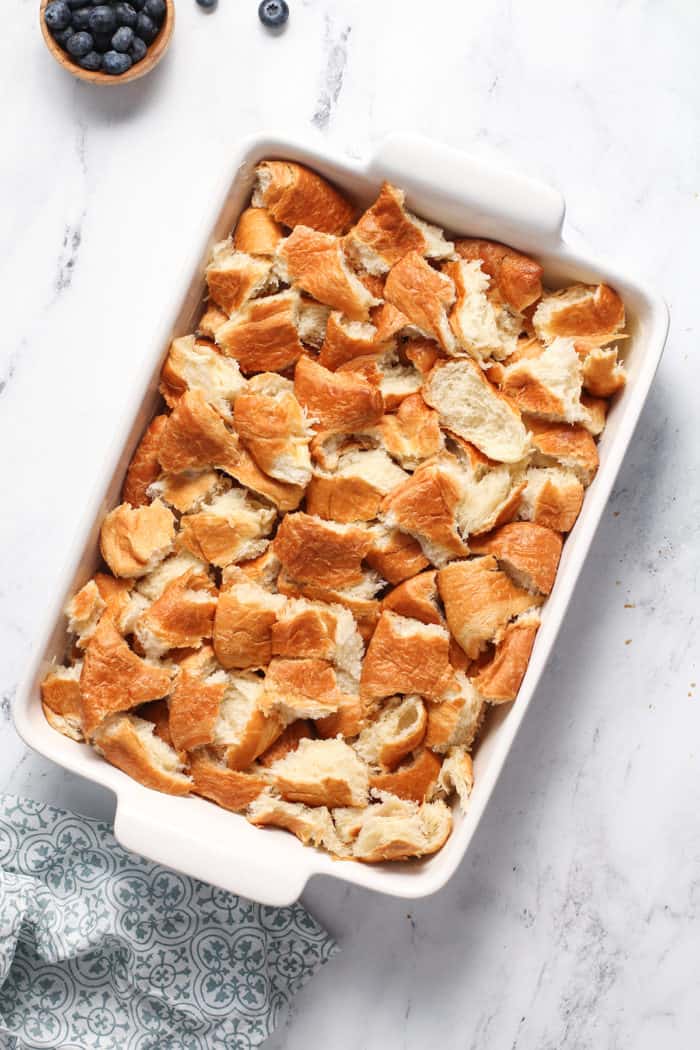 Torn pieces of croissants in a white baking dish, set on a marble countertop