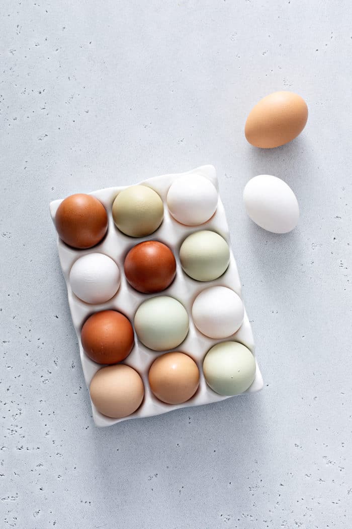 Overhead view of 14 eggs in varying colors on a light gray countertop