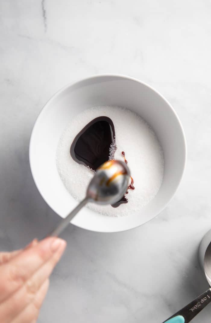 Spoonful of molasses being added to a white bowl filled with granulated sugar