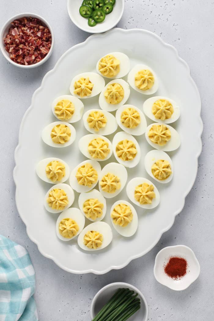 Assembled deviled eggs on a white platter, waiting for garnishes