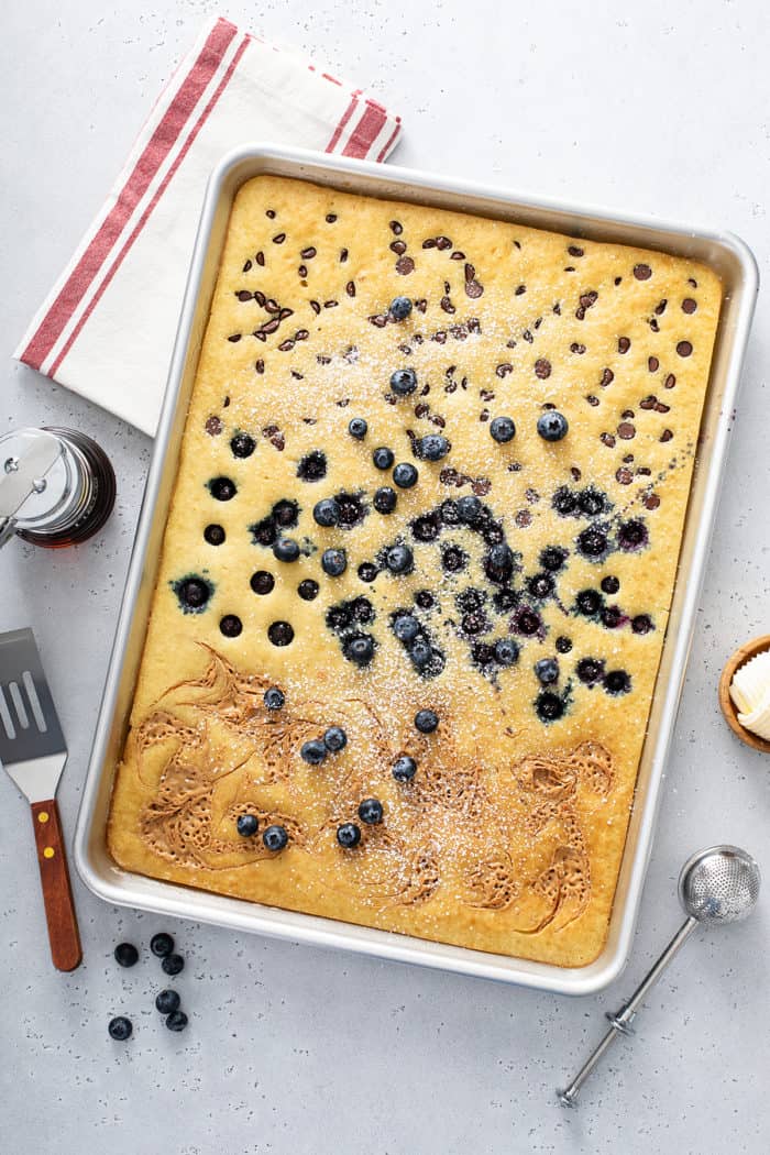 Baked sheet pan pancakes topped with peanut butter, blueberries, and chocolate chips