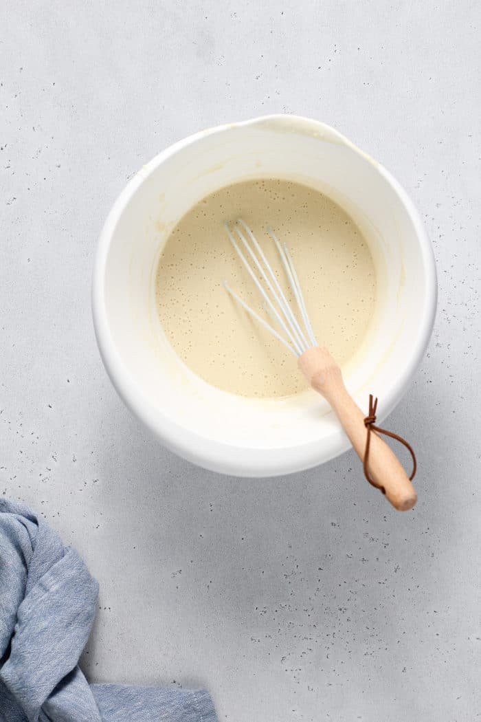 Whisk stirring bisquick waffle batter in a white mixing bowl
