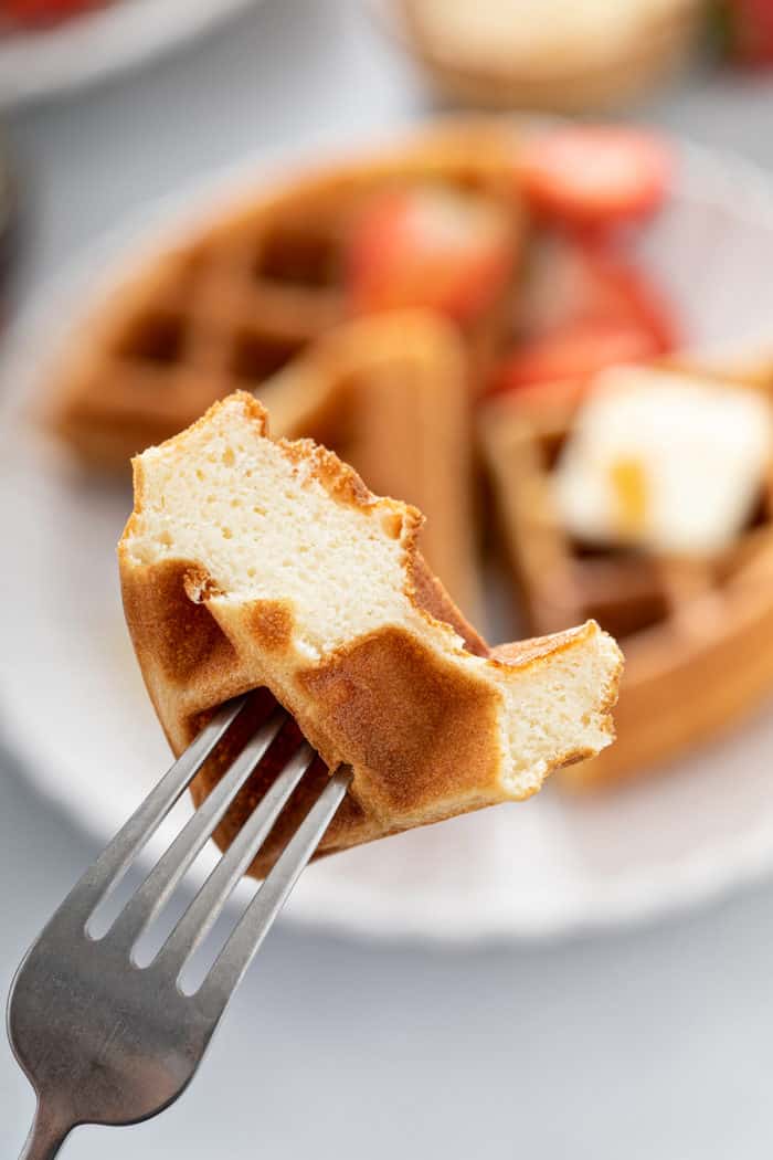 Fork holding up a bite of bisquick waffle to the camera to show the interior fluffy texture