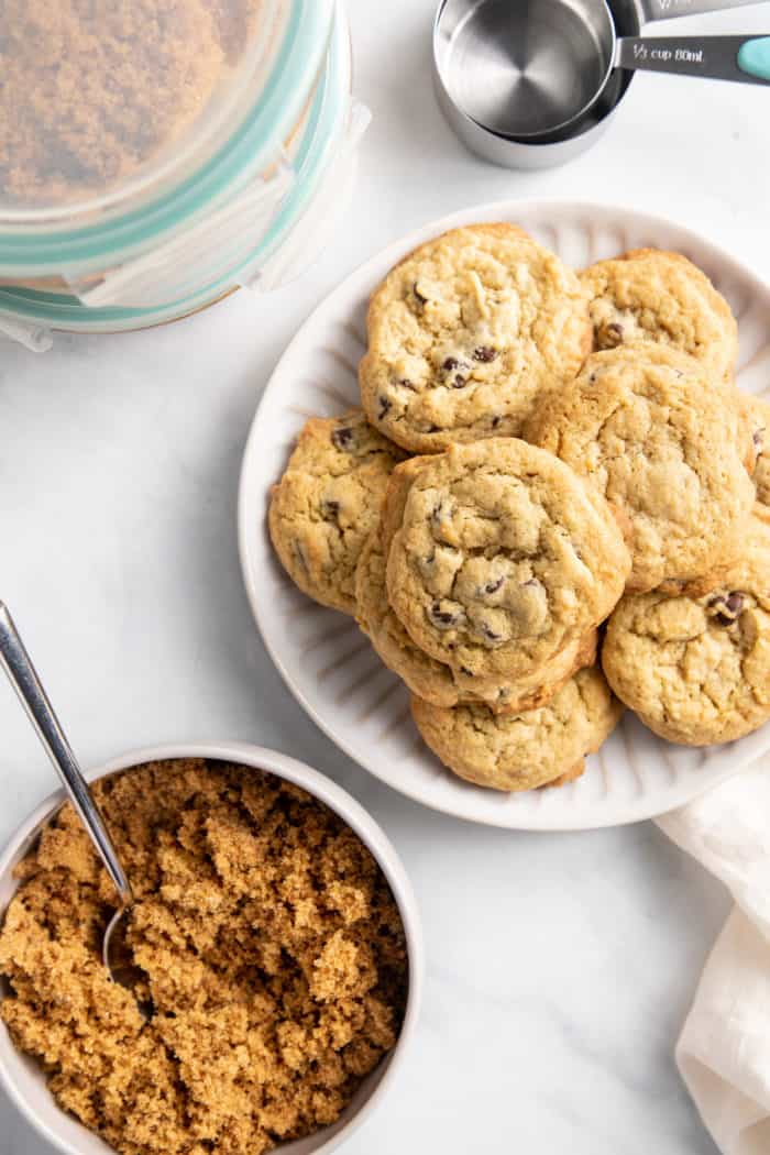Chocolate chip cookies on a white plate, set next to a bowl filled with dark brown sugar