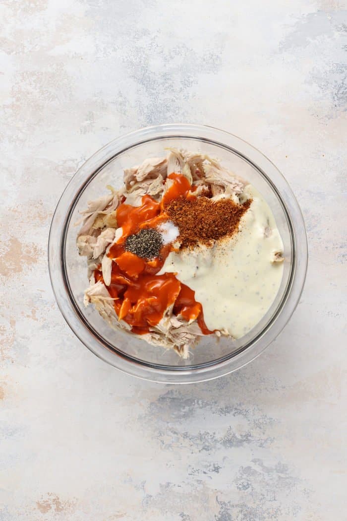 Ingredients for buffalo chicken in a glass mixing bowl, ready to be stirred together