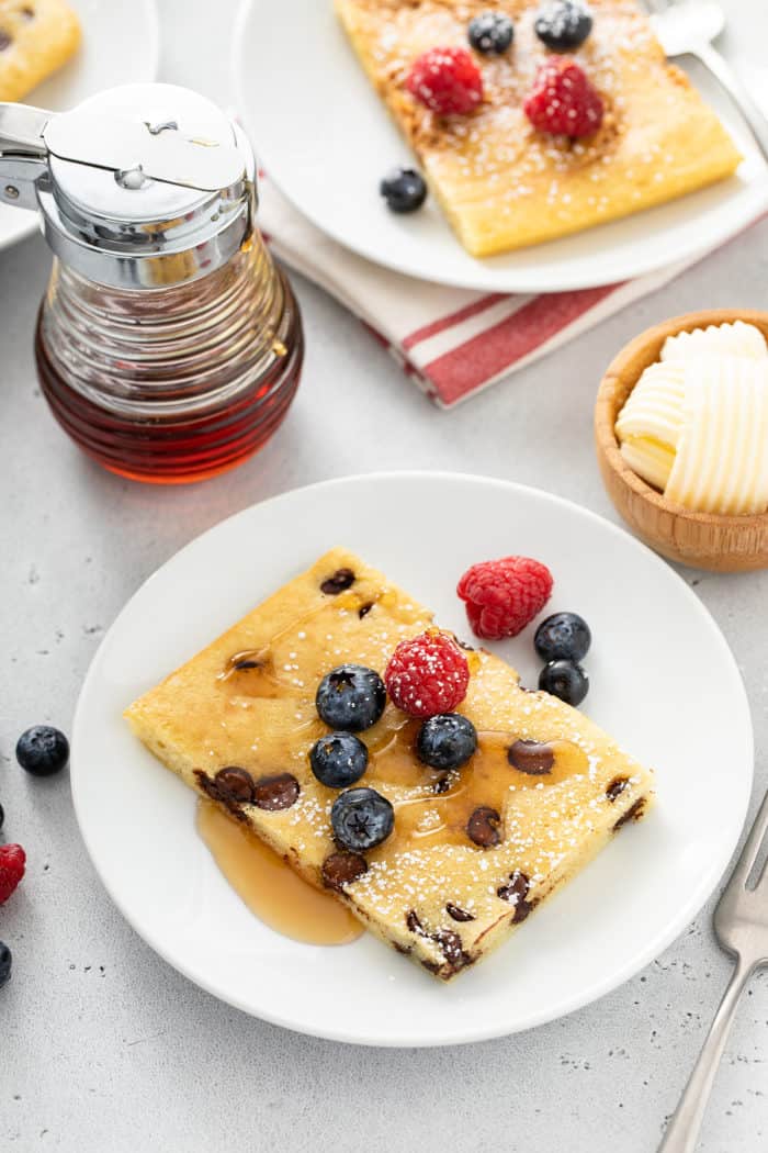 Chocolate chip sheet pan pancake topped with syrup and berries on a white plate