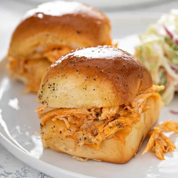 Buffalo chicken slider on a white plate with another slider and coleslaw in the background