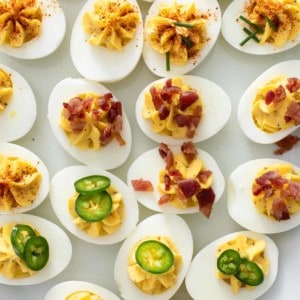 Close up of deviled eggs on a platter, topped with a variety of garnishes