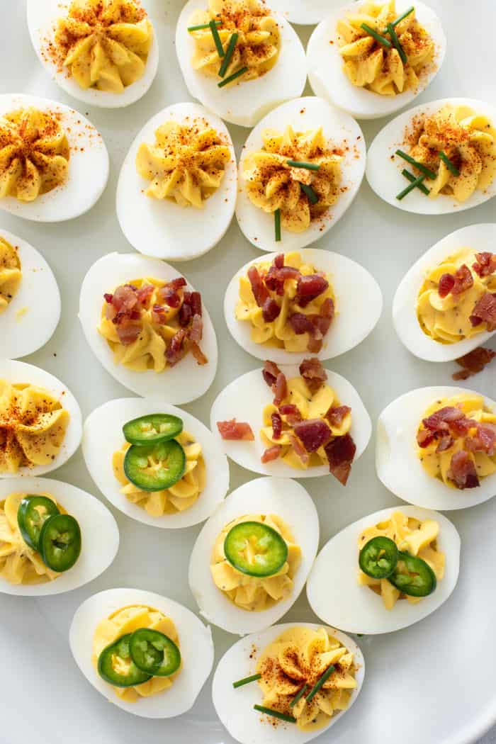 Close up of deviled eggs on a platter, topped with a variety of garnishes