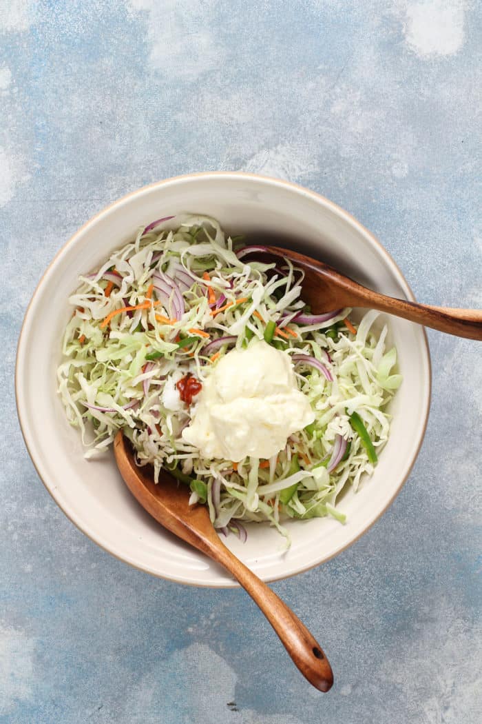Dressing ingredients on top of coleslaw vegetables in a white mixing bowl