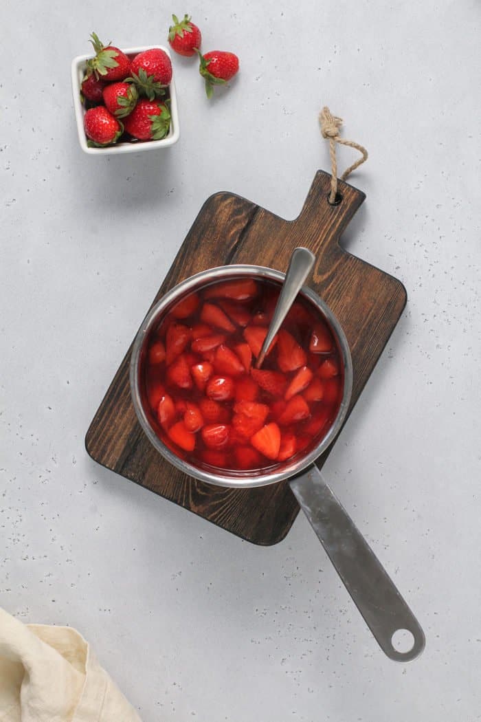 Overhead view of cooked strawberry sauce in a saucepan on a wooden cutting board