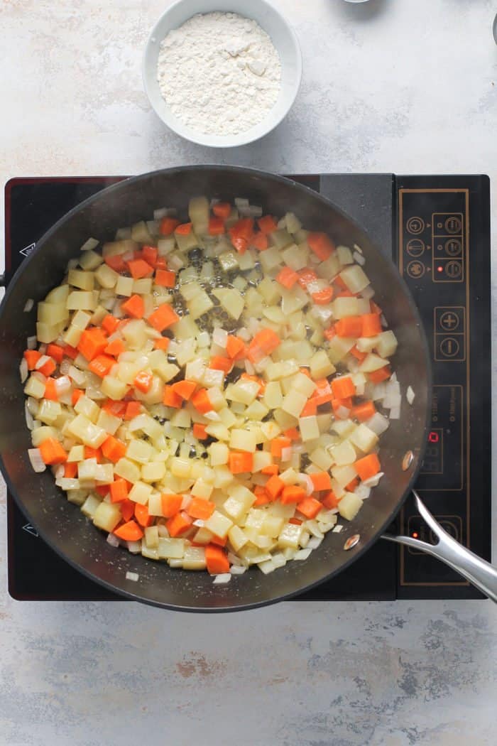 Vegetables for pot pie casserole cooking in a black skillet